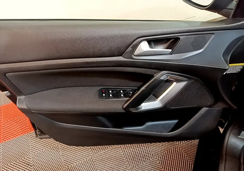Vue intérieure du panneau de porte avant gauche de la Peugeot 308 noire avec commandes électriques et poignée argentée.