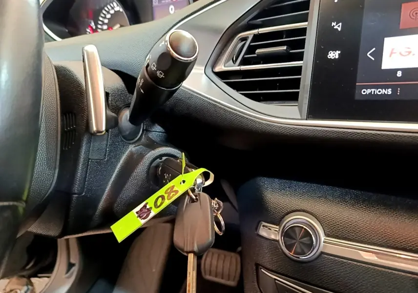 Vue rapprochée de l’intérieur noir de la Peugeot 308, montrant le volant, la clé dans le contact et l’écran tactile.