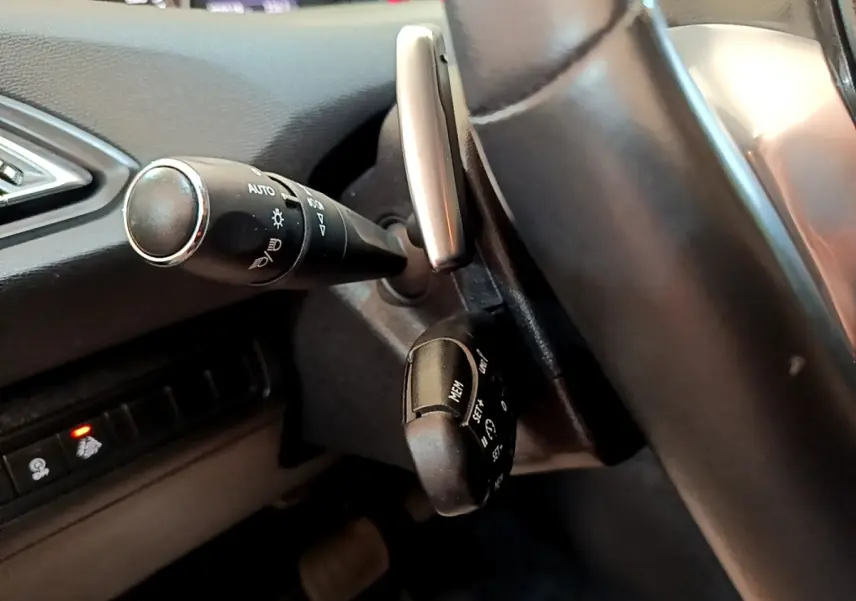 Gros plan sur les commandes au volant côté gauche d’une Peugeot 308 noire, avec leviers de clignotants et régulateur de vitesse.