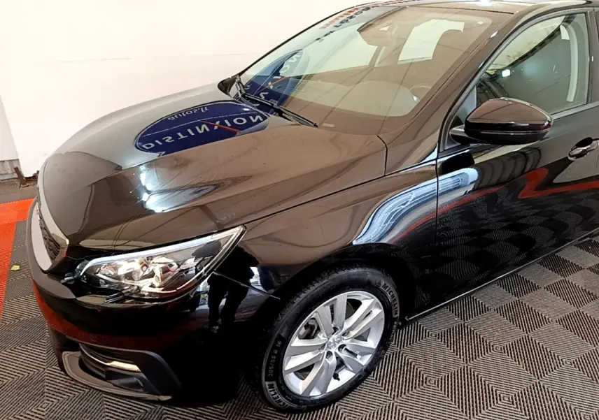 PEUGEOT 308 noir vue 3/4 avant droit, avec phares allumés et jantes alliage argentées visibles.