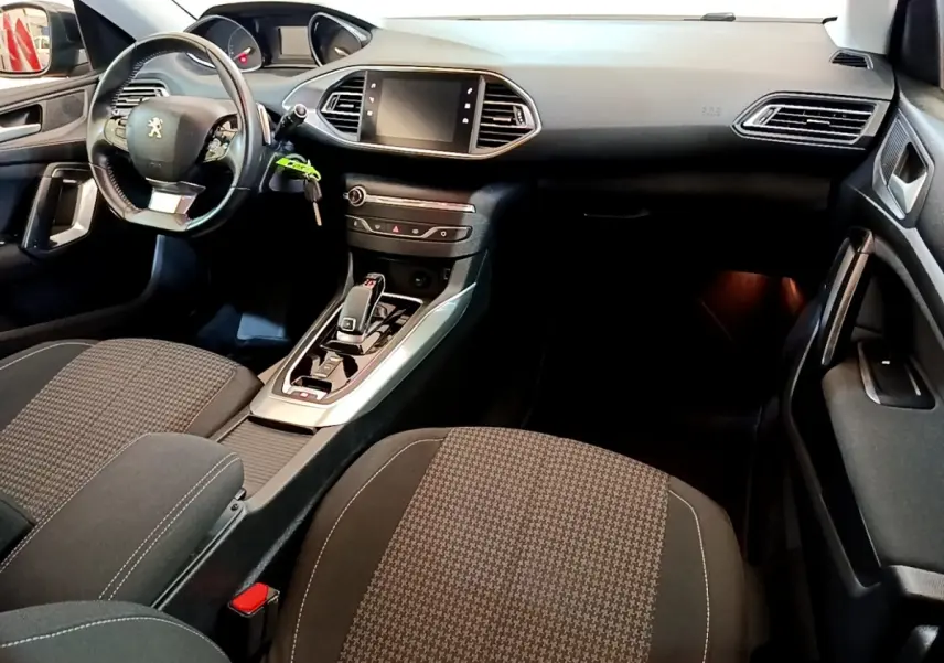Vue intérieure avant droite de la Peugeot 308 noire, montrant le tableau de bord avec écran tactile et volant cuir multifonctions.