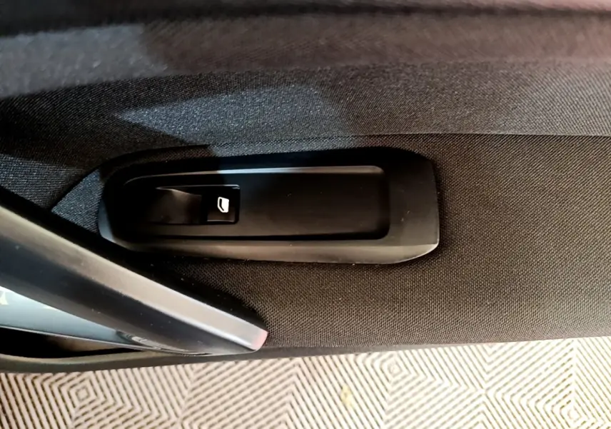 Gros plan sur la commande d’ouverture de coffre intégrée à la garniture intérieure noire d’une Peugeot 308.