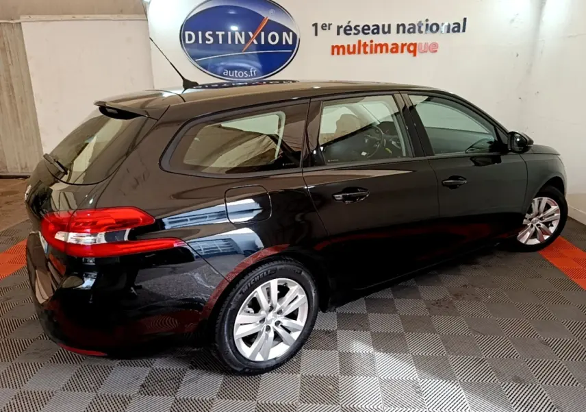 Peugeot 308 noir vue 3/4 arrière droit, avec feux arrière rouges et jantes argentées dans un showroom.