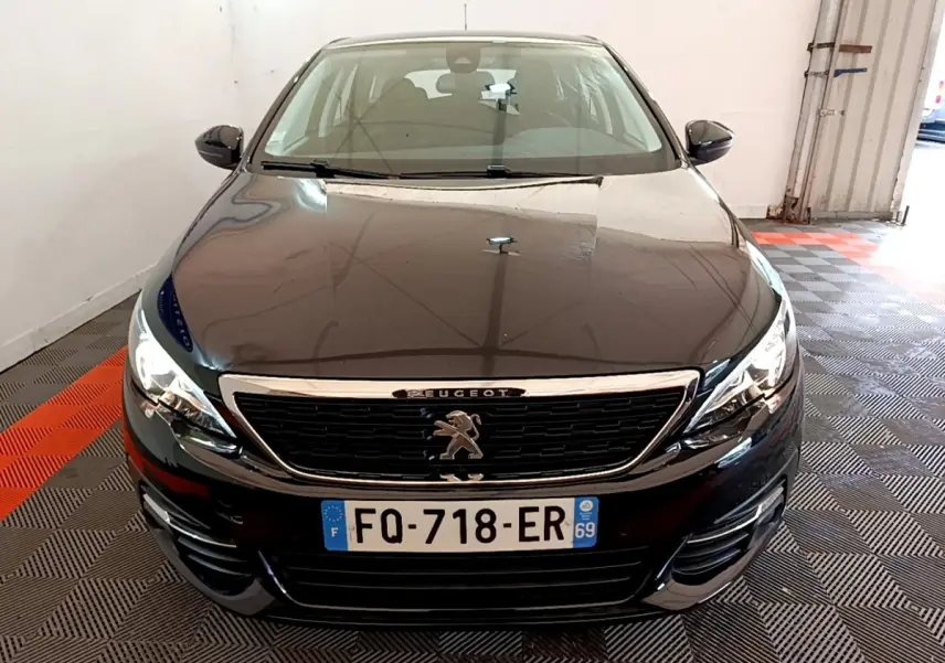 Peugeot 308 noire vue de face dans un garage, avec calandre chromée et phares allumés.
