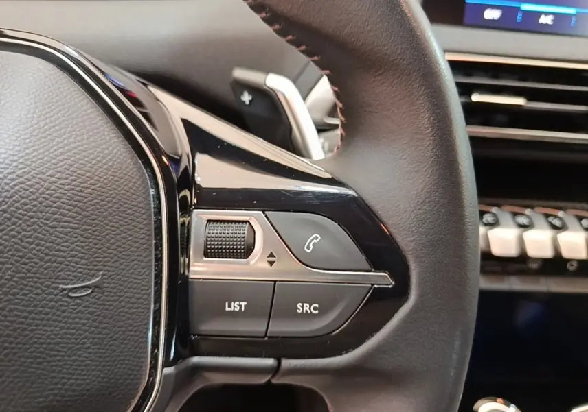 Gros plan sur les commandes gauche du volant cuir noir du Peugeot 3008 2022, avec tableau de bord et écran tactile en arrière-plan.