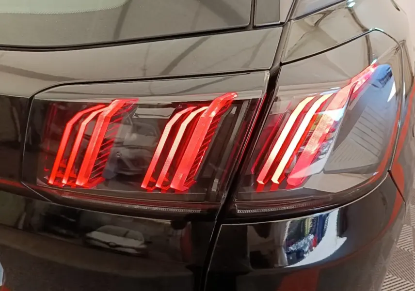 Gros plan sur les feux arrière rouges du Peugeot 3008 noir, vue de l'arrière droite avec reflets sur la carrosserie.