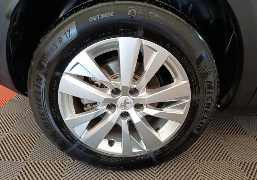 Gros plan sur la roue avant droite d’un Peugeot 3008 noir, jante alliage argentée avec logo Peugeot central.