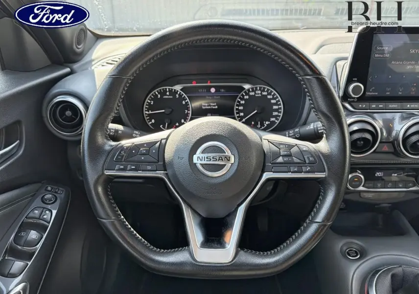 Vue intérieure centrée sur le volant cuir Nissan avec commandes multifonctions et tableau de bord digital.