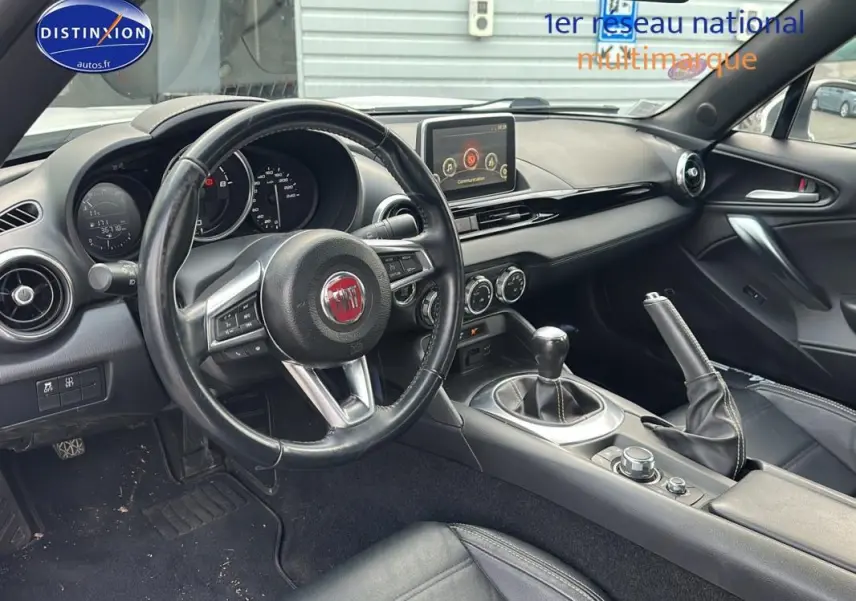 Intérieur noir de la FIAT 124 Spider 2017 vu côté conducteur, volant cuir multifonctions et boîte manuelle visible.