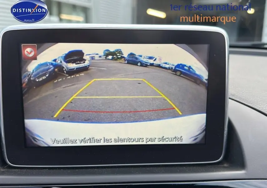 Écran tactile montrant la caméra de recul d'une Fiat 124 Spider blanche, vue arrière avec lignes de guidage colorées.