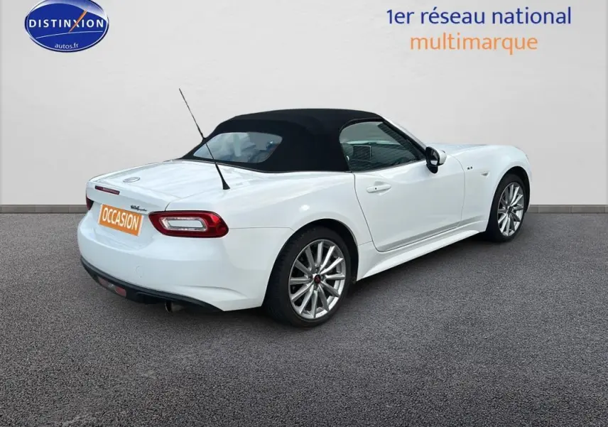 Fiat 124 Spider blanc vue 3/4 arrière droit avec capote noire et jantes alliage 17 pouces.