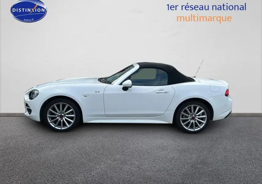 Profil côté gauche d'une FIAT 124 Spider blanche avec capote noire et jantes alliage 17 pouces.