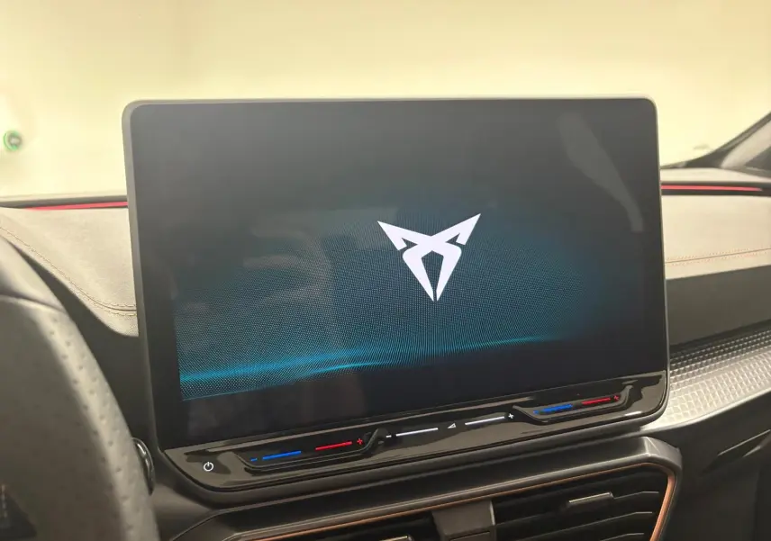 Écran tactile central allumé avec logo CUPRA, tableau de bord noir et surpiqûres orange dans l'habitacle du Formentor.