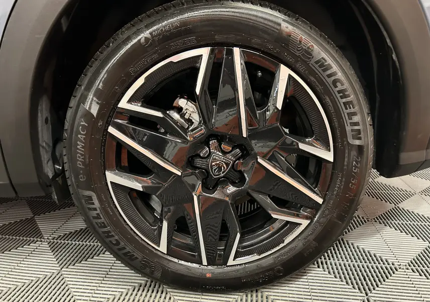 Gros plan sur la jante noire et argentée du PEUGEOT 3008 III HYBRID 145 e-DSC6 ALLURE bleu Ingaro, pneu Michelin visible.