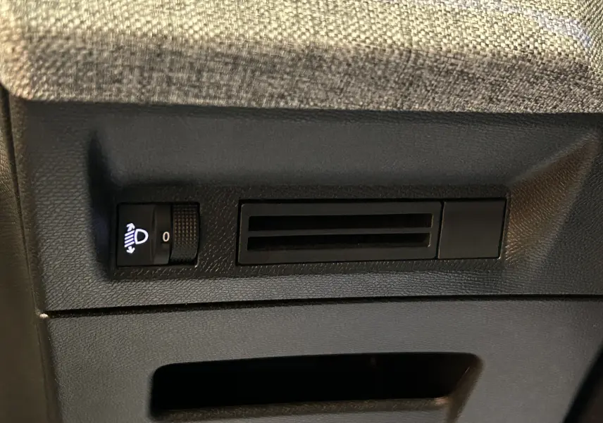 Gros plan sur la commande de réglage des phares et la ventilation sous le tableau de bord d'une Peugeot 3008 hybride 2025.