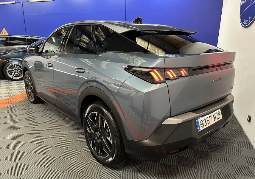 Vue 3/4 arrière droite du Peugeot 3008 III Hybrid 145 bleu Ingaro avec feux arrière LED et jantes noires en concession.