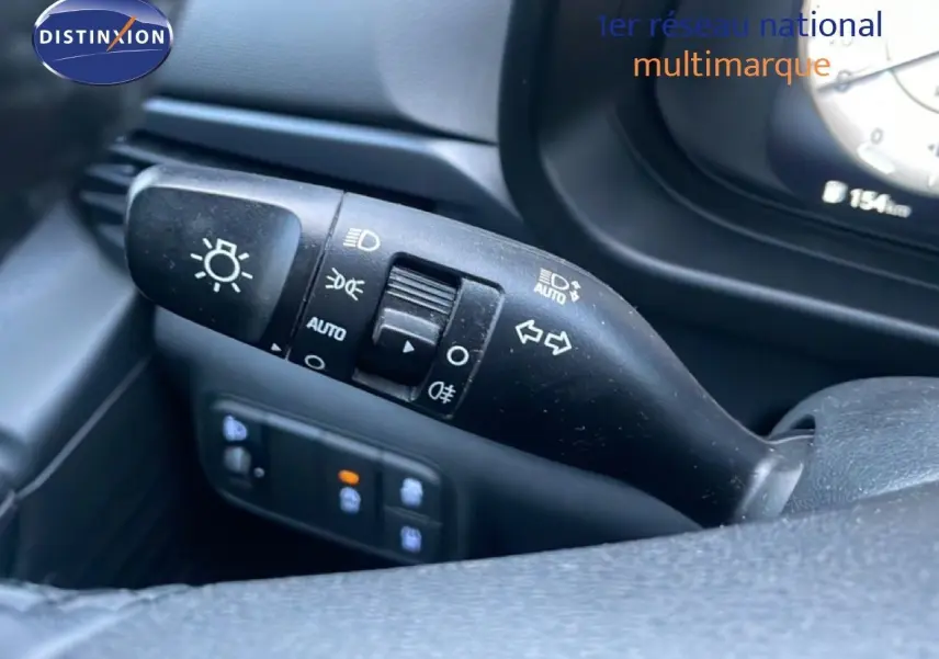 Gros plan sur la commande de clignotants et phares à gauche du volant dans l’habitacle d’une Hyundai i20 blanche.