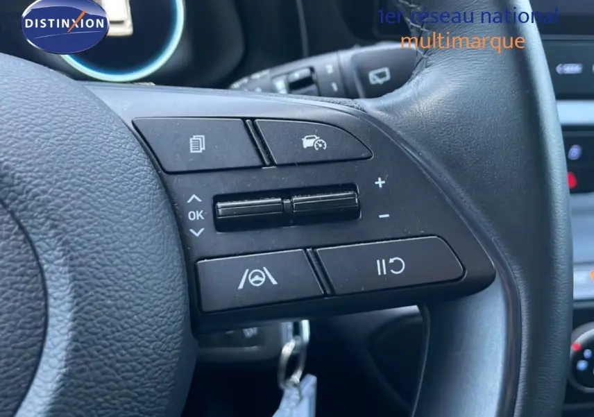 Gros plan sur les commandes au volant en cuir noir de la Hyundai i20 blanche, mettant en valeur les boutons de régulateur de vitesse.