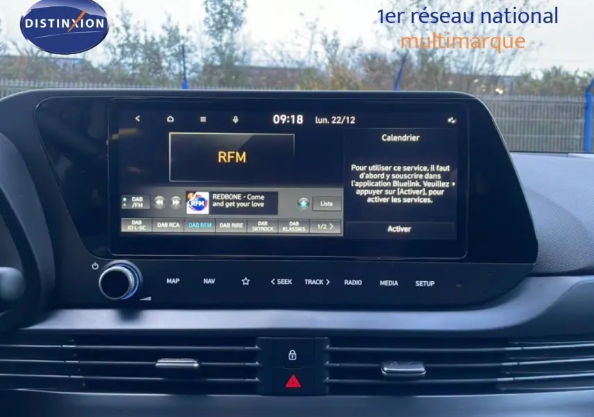 Vue intérieure centrée sur l'écran tactile multimédia de la Hyundai i20 blanche, affichant la radio et le calendrier.