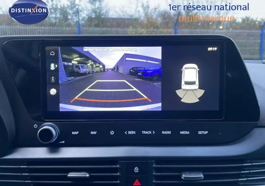 Écran tactile intérieur montrant la caméra de recul et l’aide au stationnement de la Hyundai i20 blanche, vue de face.