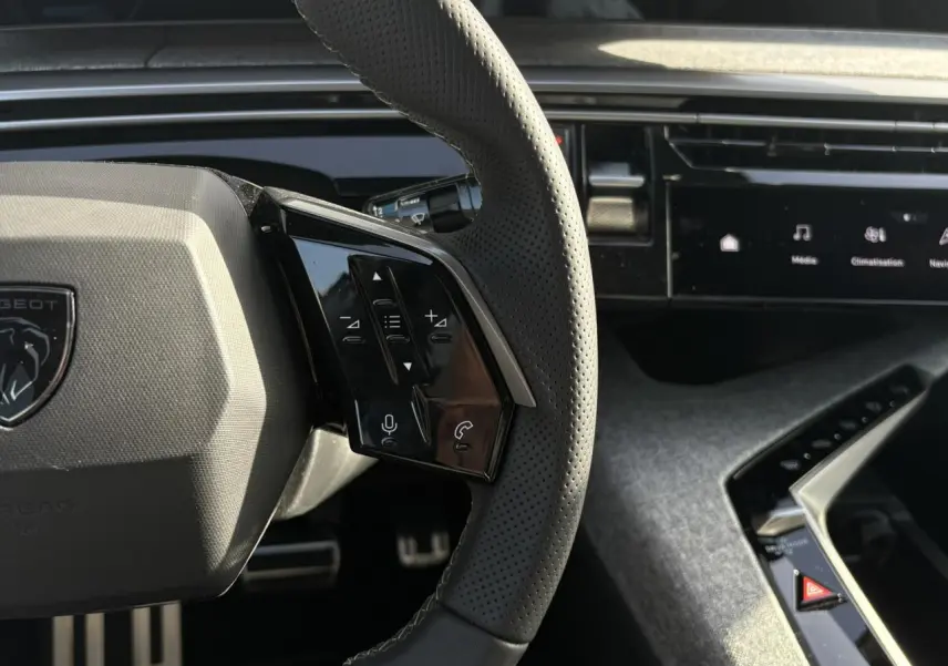 Gros plan sur le volant perforé noir avec commandes intégrées et partie de la planche de bord du Peugeot 3008 Hybrid 2025.