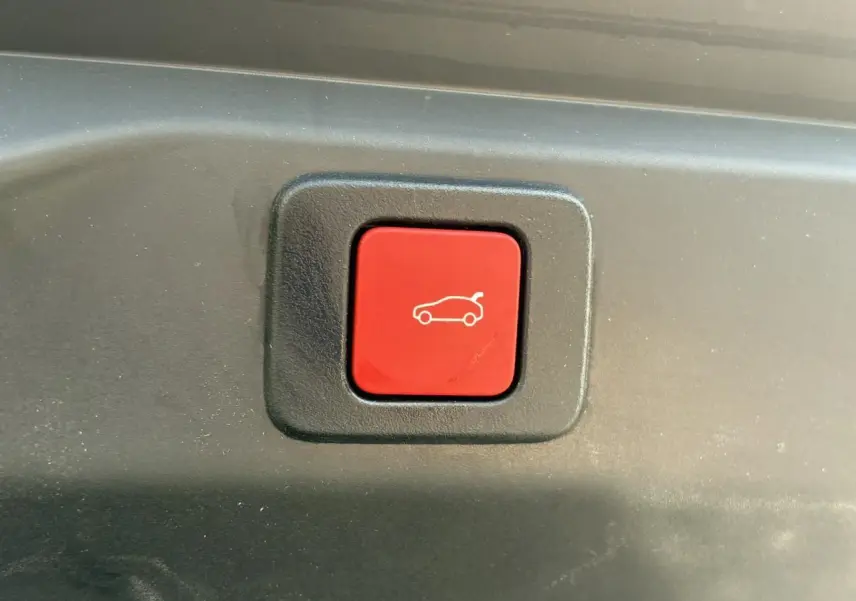 Bouton rouge de déverrouillage du hayon sur le coffre d'un Peugeot 3008 Hybrid 2025 gris Titane.