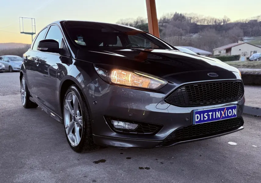 Vue 3/4 avant d'une Ford Focus gris métallisé 2018 avec phares allumés et calandre noire distinctive.