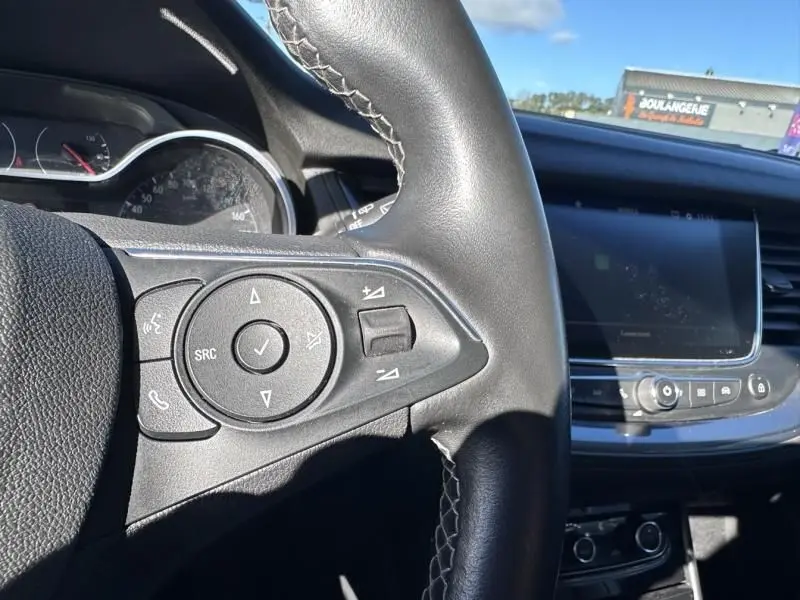 Gros plan sur le volant noir et les commandes multifonctions de l’Opel Grandland X blanc, vue intérieure côté conducteur.