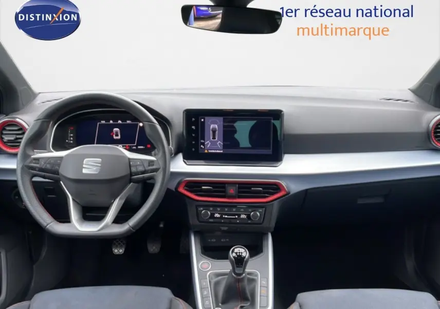Vue intérieure avant du tableau de bord du SEAT Arona 2025 avec volant multifonction et touches rouges autour des aérateurs.
