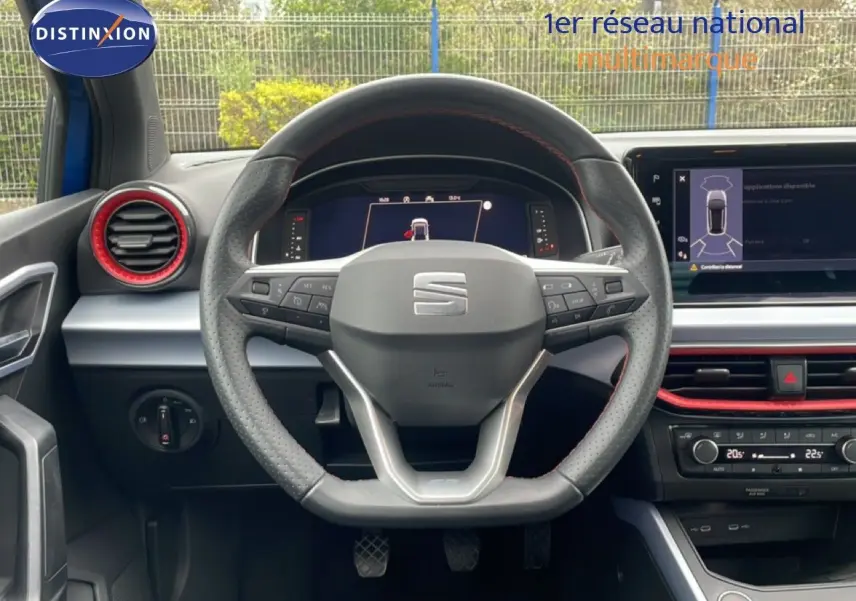 Vue intérieure centrée sur le volant perforé de la SEAT Arona 2025, avec détails rouges et écran numérique visible.