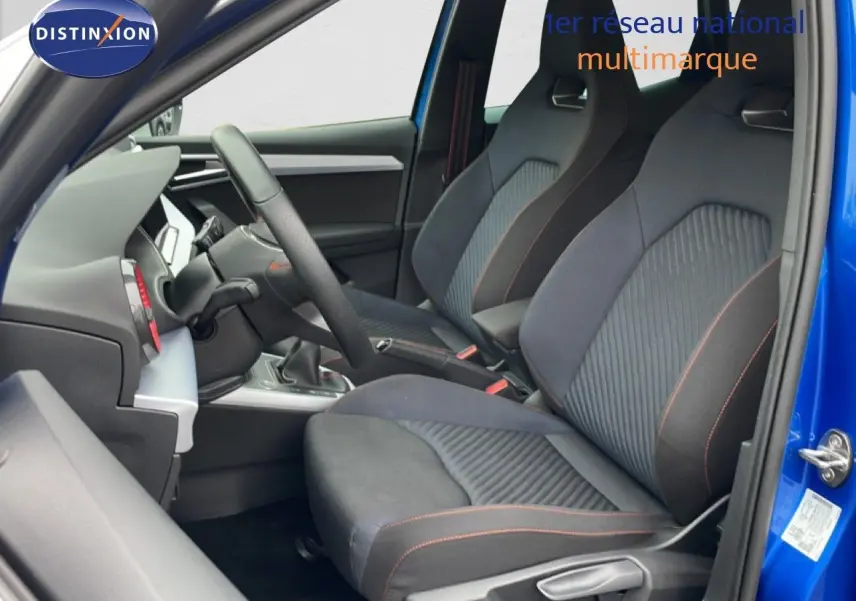 Vue intérieure côté conducteur du SEAT Arona bleu saphir, sièges sport tissu noir avec surpiqûres orange.