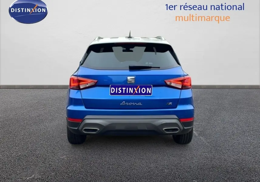 Vue arrière d'un SEAT Arona bleu saphir métal avec toit blanc, affichant ses feux et double sortie d'échappement.