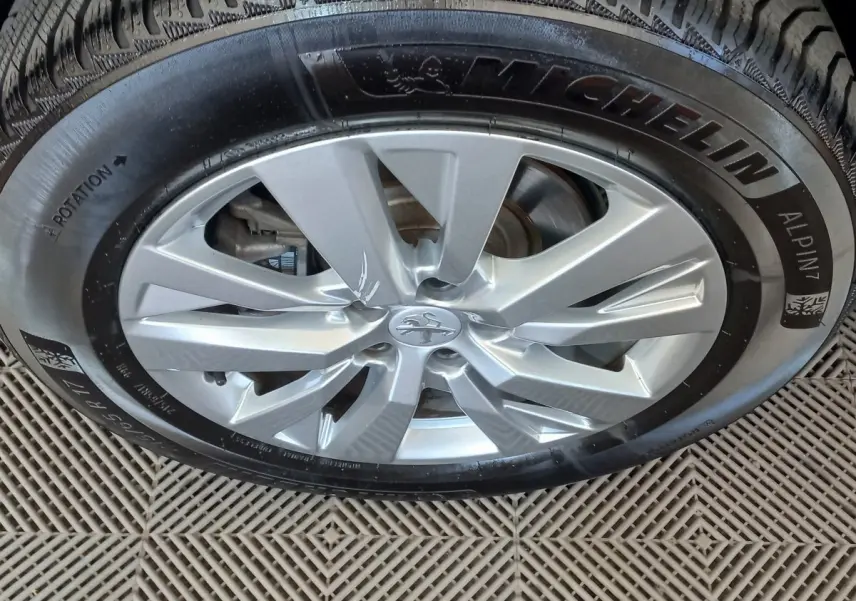 Gros plan sur la jante argentée et le pneu Michelin d'un Peugeot 3008 noir, vue de dessus.