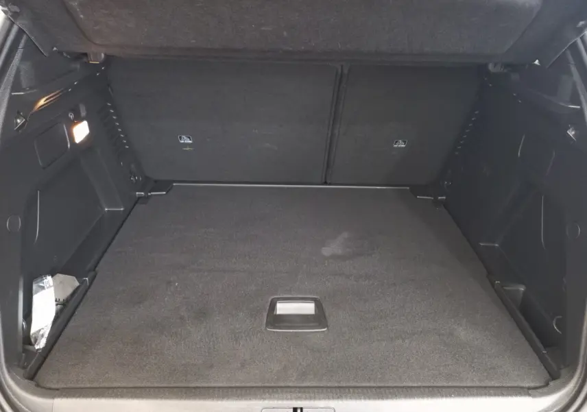 Coffre noir ouvert du Peugeot 3008 PureTech 130, vue de face montrant l'espace de chargement plat et les rangements latéraux.