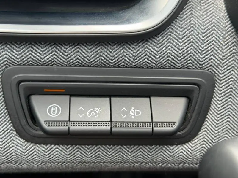 Gros plan sur les boutons de réglage de l’éclairage et verrouillage sur tissu gris à motif chevrons dans une Renault Clio gris schiste.