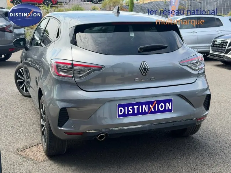 Vue 3/4 arrière droite d'une Renault Clio gris schiste avec feux arrière LED et sortie d'échappement chromée visible.
