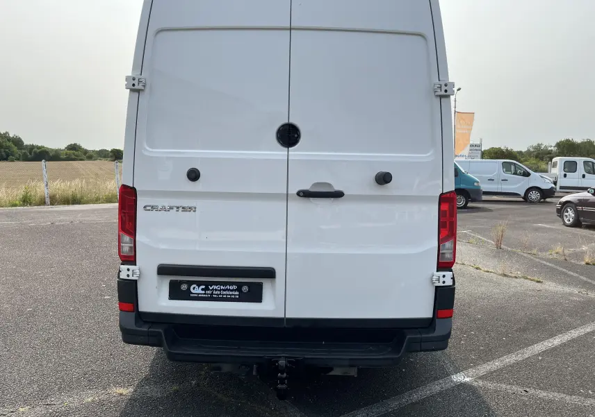 Vue arrière d'un fourgon Volkswagen Crafter blanc avec portes battantes et attelage de remorque visible.