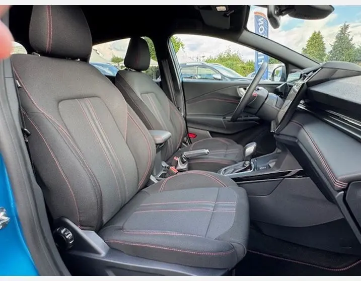 Intérieur avant droit de la Ford Puma 2025 bleu Aqua, sièges sport noirs avec surpiqûres rouges ST Line et console centrale moderne.