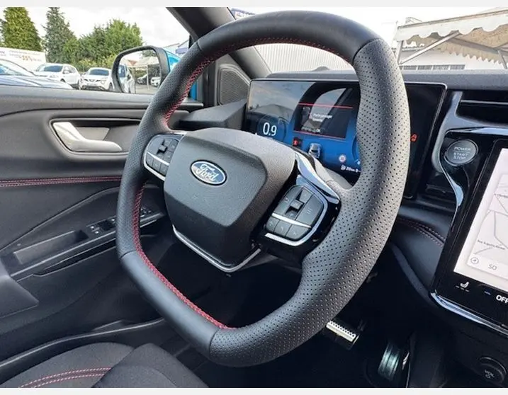 Vue rapprochée du volant perforé avec surpiqûres rouges du Ford Puma bleu Aqua Blue, tableau de bord numérique visible.