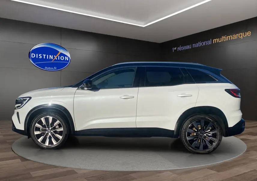 Vue de profil côté gauche du Renault Austral blanc nacré avec toit noir et jantes alu 19 pouces dans un showroom.