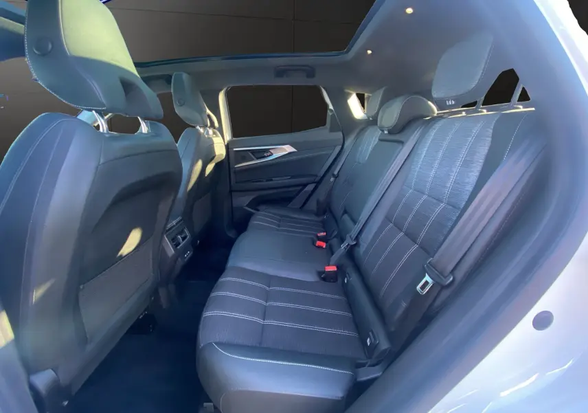 Vue intérieure arrière droite du Renault Austral blanc nacré, montrant les sièges noirs et le toit panoramique lumineux.