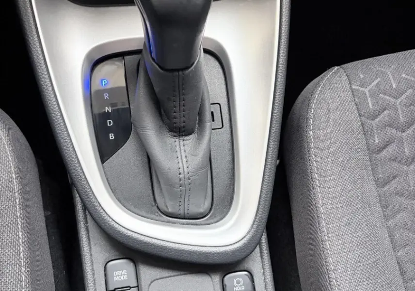 Gros plan sur la console centrale avec levier de vitesse automatique en cuir noir et boutons de mode de conduite, sièges gris.