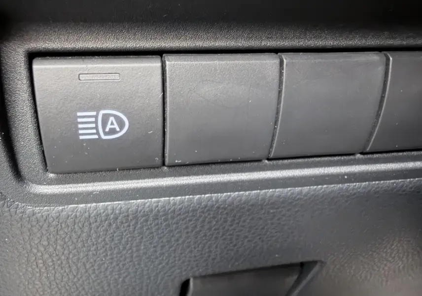 Gros plan sur le bouton de commande des feux automatiques dans l’habitacle noir de la Toyota Yaris Cross 2024 gris clair.