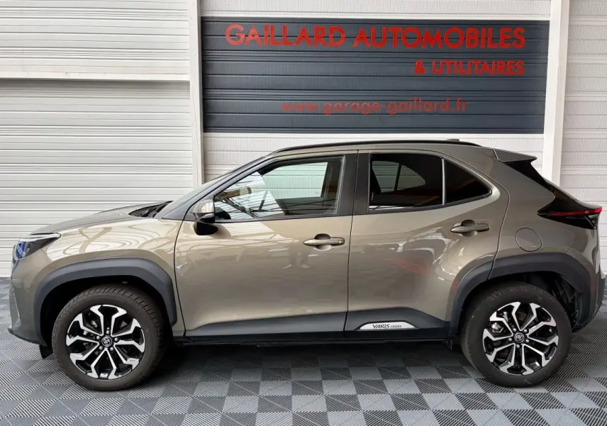 Profil droit de la Toyota Yaris Cross gris clair 2024 avec jantes alliage noires et logo Yaris Cross sur bas de caisse.