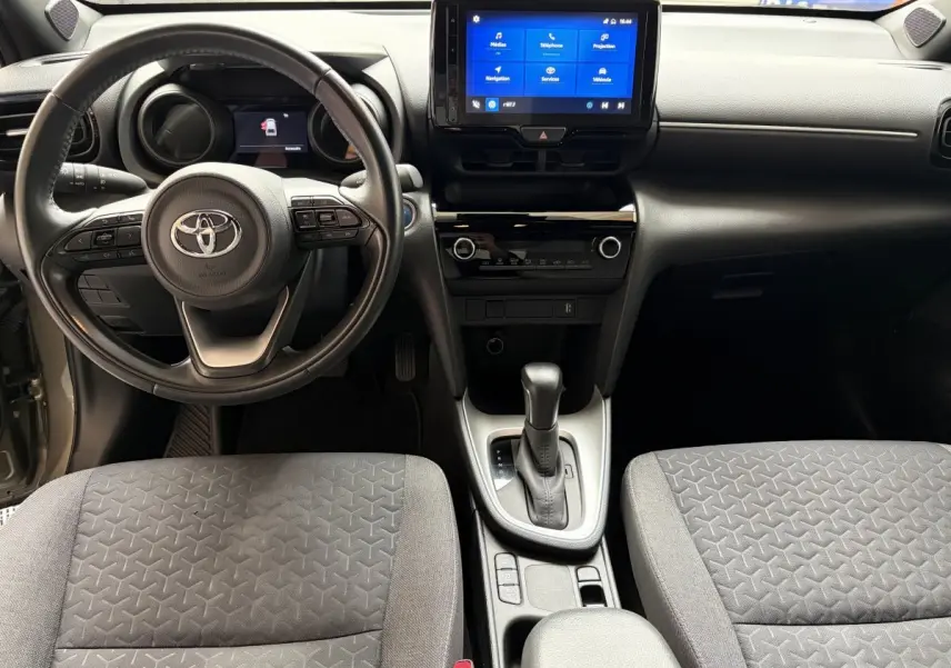 Vue intérieure avant centrée sur le volant cuir et l’écran tactile du tableau de bord de la Toyota Yaris Cross 2024.