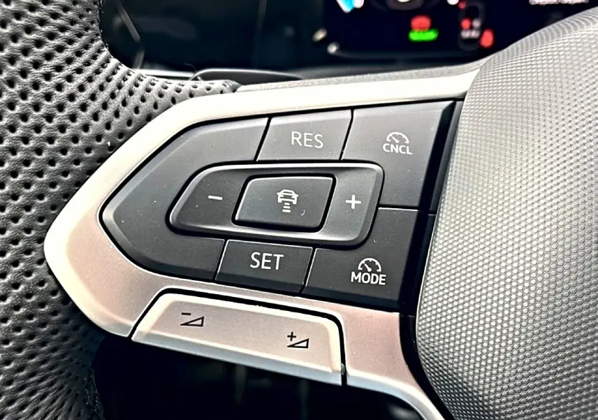 Gros plan sur les commandes du volant côté gauche d’une Volkswagen Golf noire 2026, avec boutons de régulateur de vitesse.