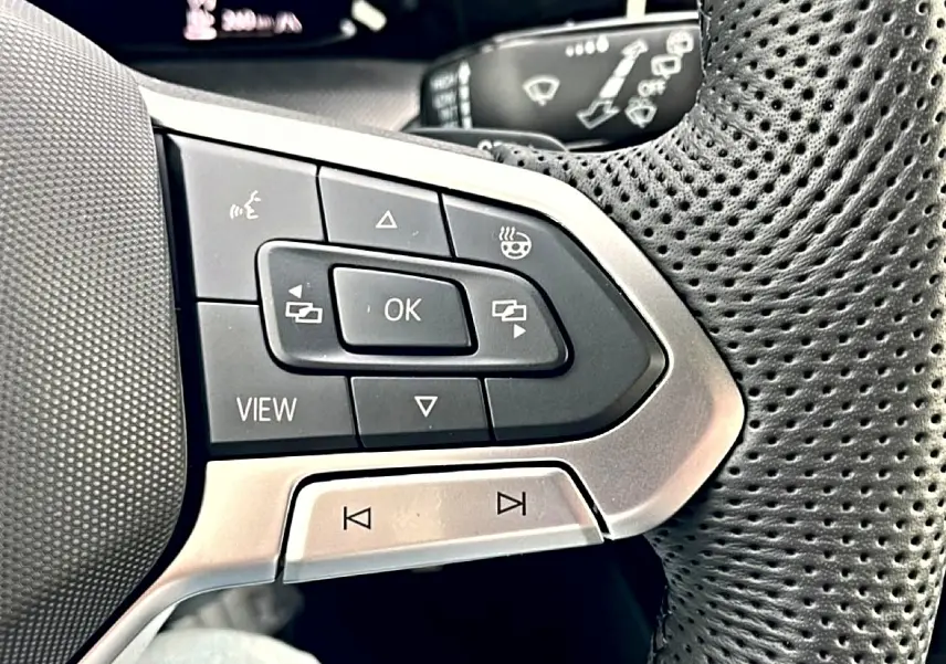 Gros plan sur les commandes multifonctions gauche du volant perforé noir de la Volkswagen Golf 2026.