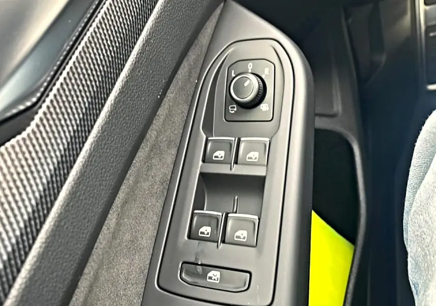 Vue rapprochée des commandes de réglage des rétroviseurs et vitres côté conducteur d'une Volkswagen Golf noire 2026.
