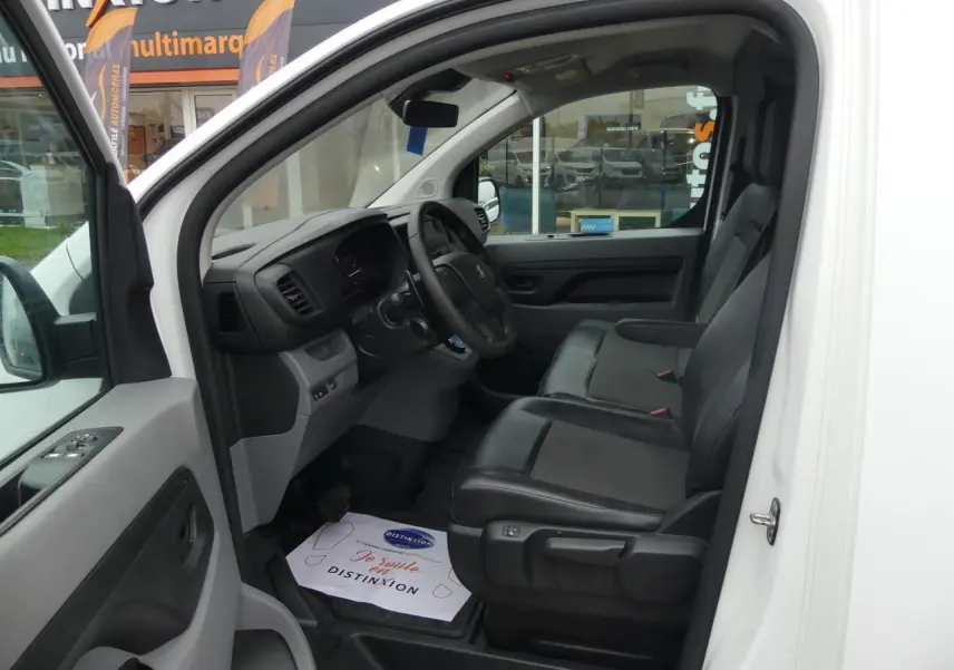 Vue intérieure côté conducteur du Peugeot Expert Fourgon blanc, montrant les sièges avant en tissu et tableau de bord noir.