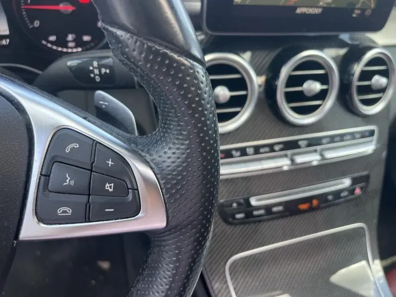 Gros plan sur le volant cuir noir perforé et la console centrale carbone du Mercedes GLC Coupé blanc diamant designo 2016.